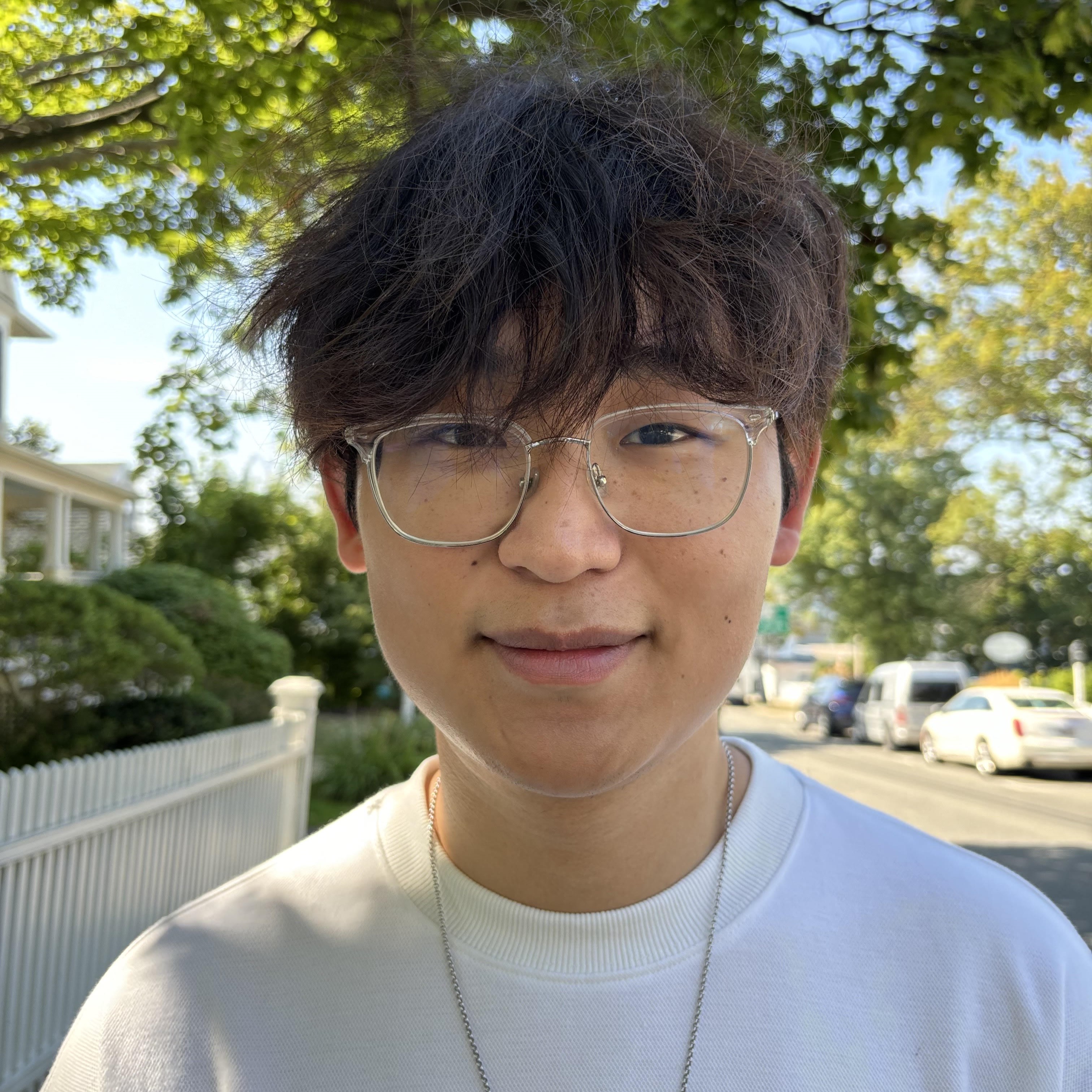 Headshot of man with dark hair and glasses, wearing a white t-shirt smiling for the camera